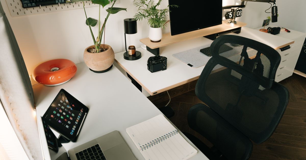 A stylish home office setup featuring tech gadgets, a monitor, a tablet, and decorative plants in a minimalist design.