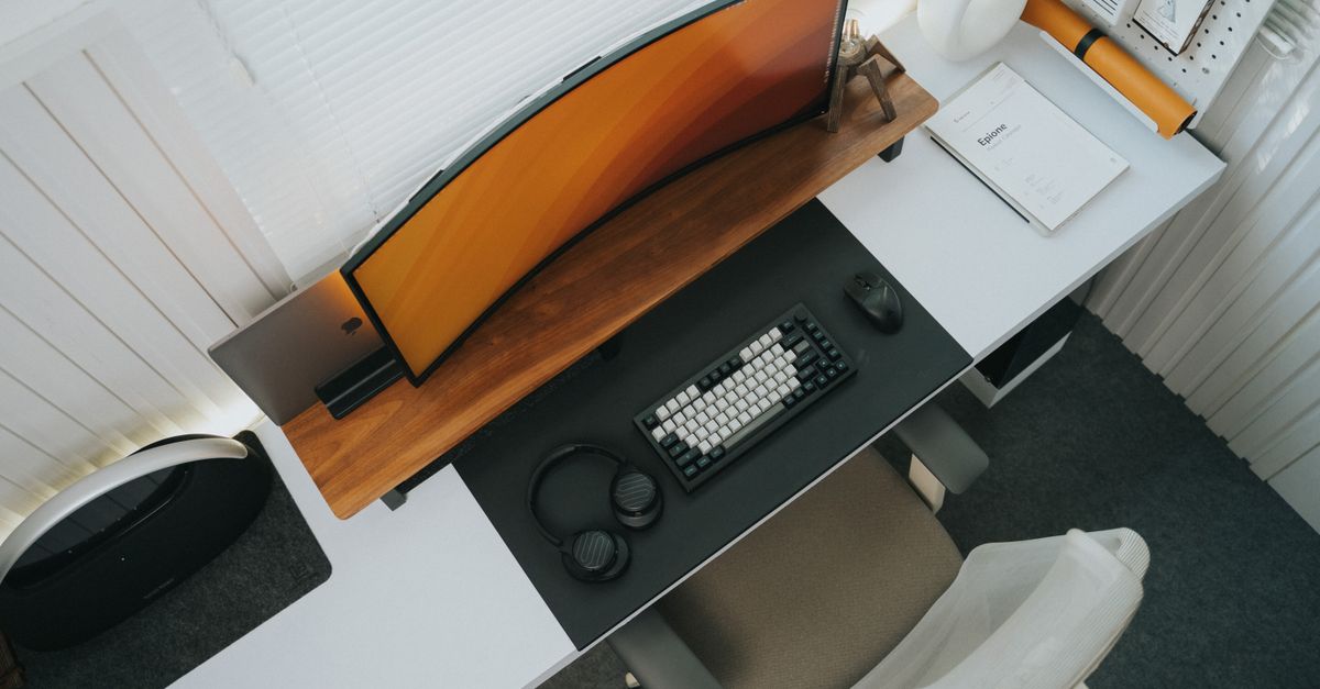 Top view of a stylish modern office desk setup featuring a curved monitor and keyboard.